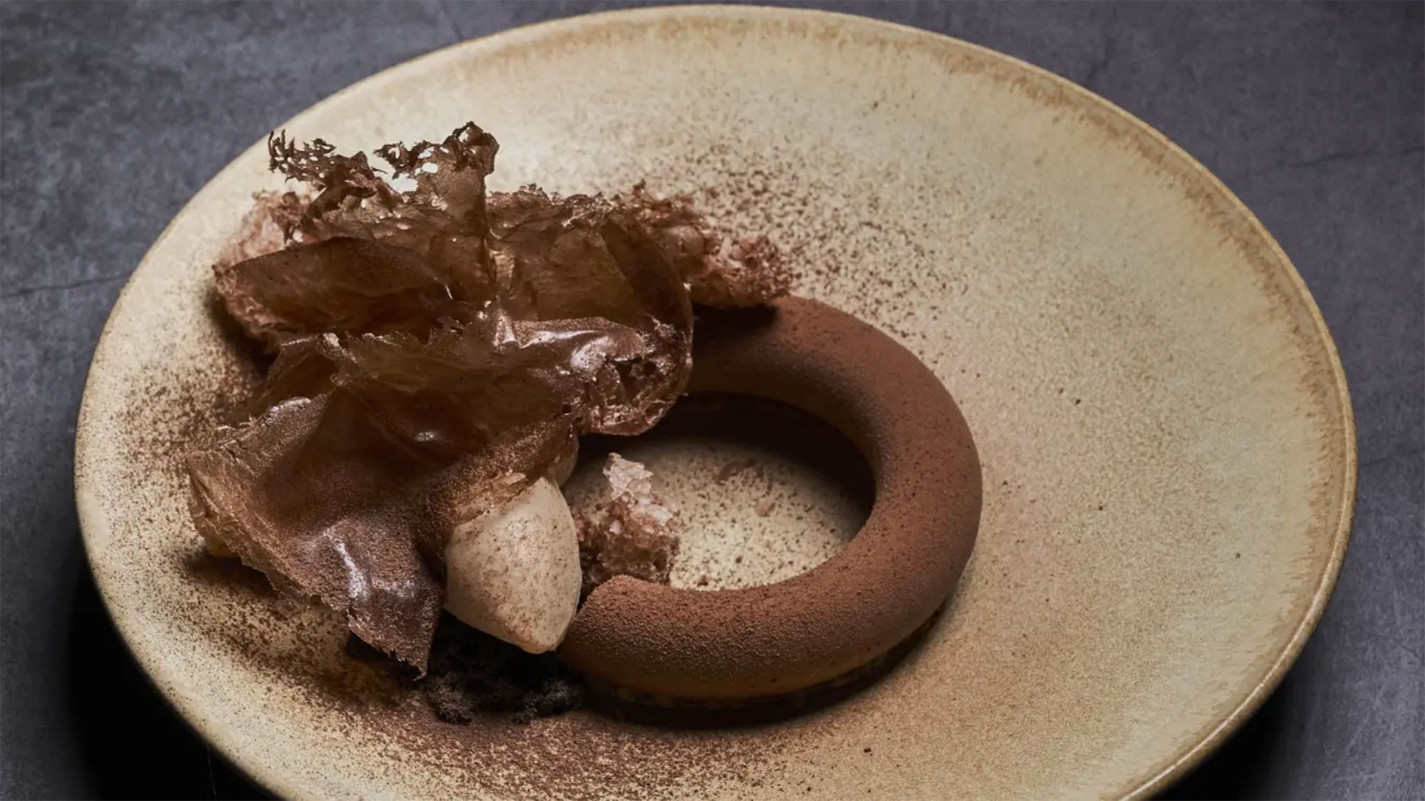 Dessert al piatto di alta pasticceria con mousse al cioccolato, decorazioni croccanti e finitura effetto velluto